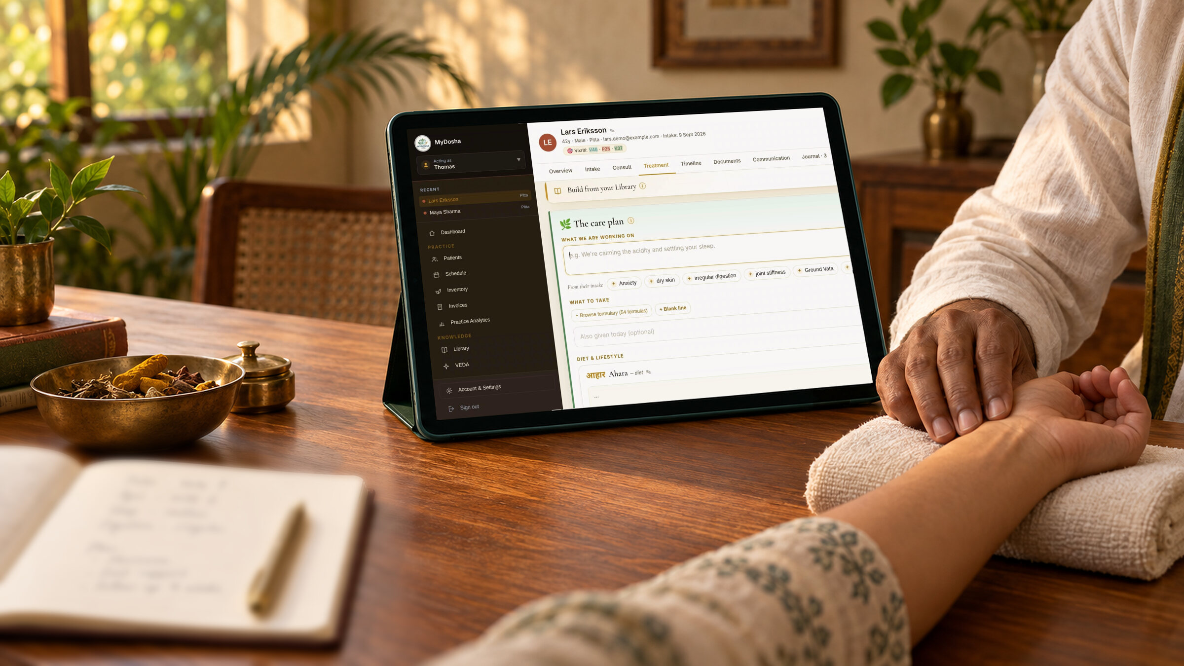 Ayurvedic practitioner taking a patient’s pulse, with a MyDosha care plan open on a tablet