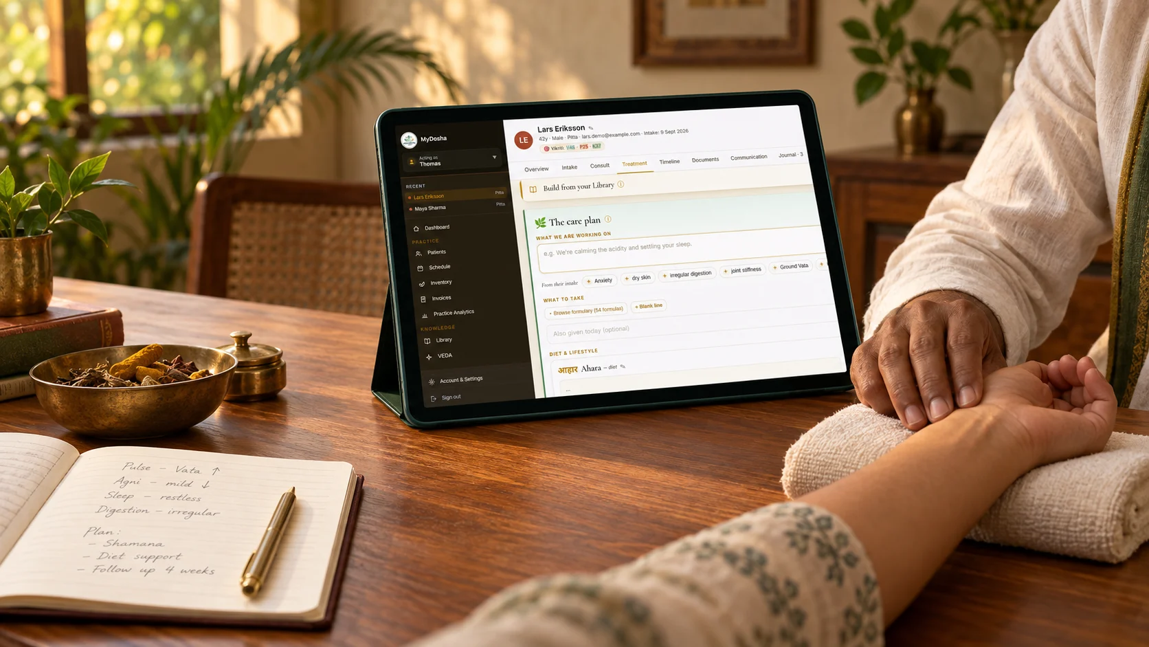 Ayurvedische behandelaar voelt de pols van een cliënt, met een MyDosha-behandelplan open op een tablet